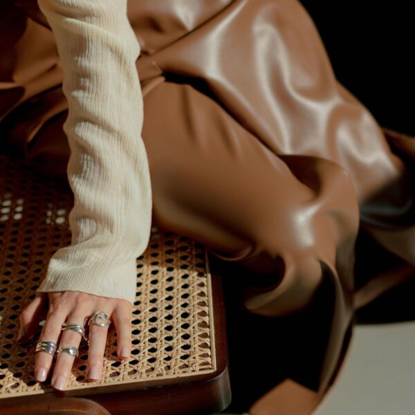 Girl in brown leather trousers and silver rings on a rattan chair