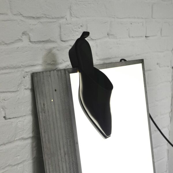 Black leather sabots on an overhead projector leaning against a white brick wall