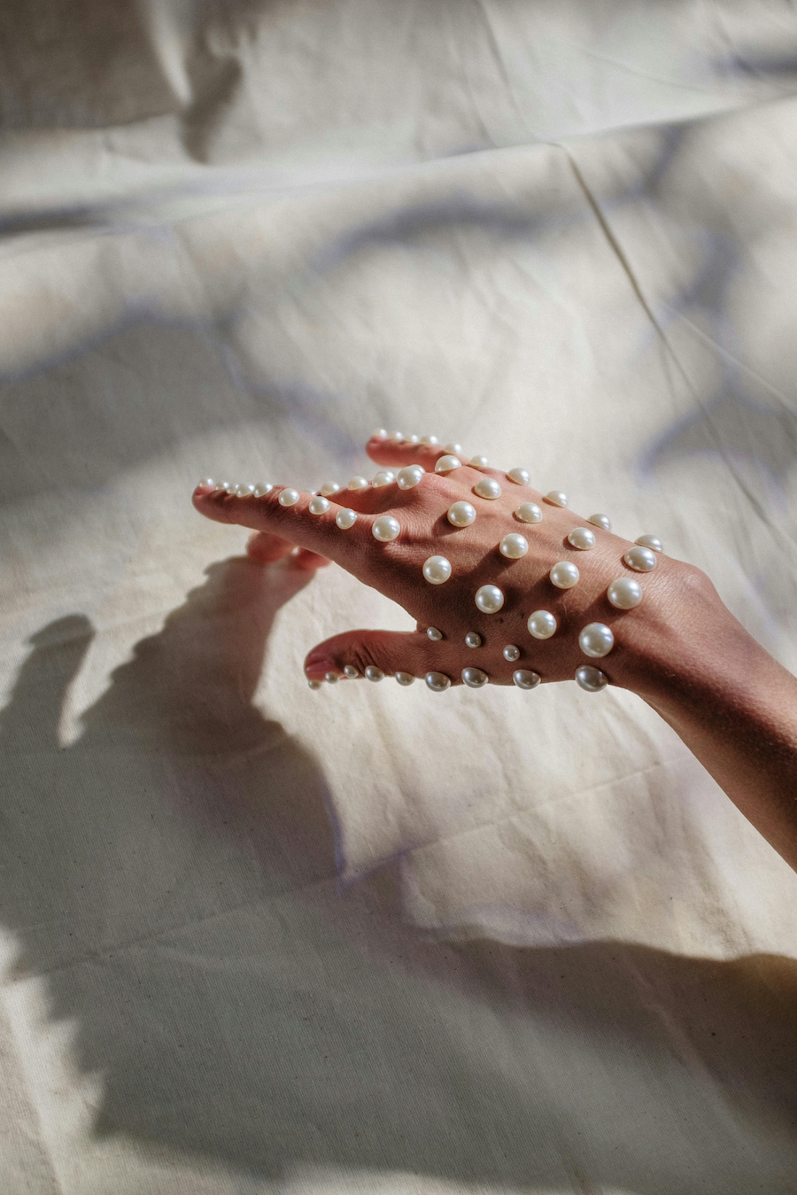 Hand with white pearls on natural fabric