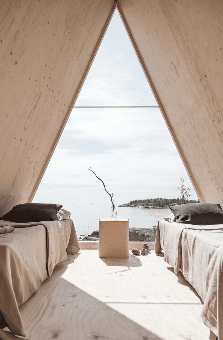 Two beds with natural linen sheets in a wood room with a big triangle window 